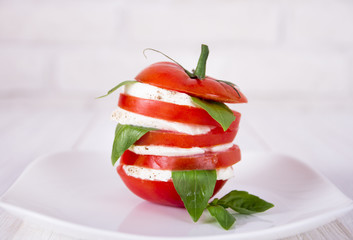 Sliced tomato and mozzarella with basil leafs on the white plate. Burger style