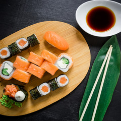 Japanese food, catering, roll plate or platter set. Sushi roll with chopsticks, ginger, soy sauce, wasabi at dark background. Top view. Flat lay