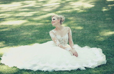 Fototapeta na wymiar Happy cute bride in white wedding dress on green grass