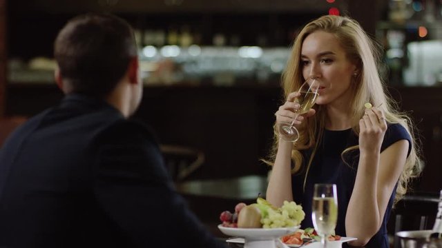romantic girl drinking champagne in restaurant and eating grapes