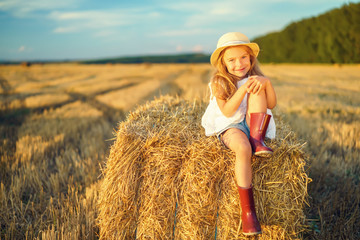 Naklejka na ściany i meble Little girl in a field with hay rolls at sunset