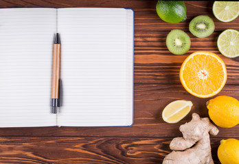 Fresh organic fruits and open blank notebook and pen on wooden background. Healthy food and healthy life concept. Top view