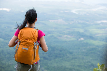 young traveler with backpack standing on the mountain peak