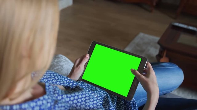 Young Woman in blue jeans sitting on couch uses Tablet PC with pre-keyed green screen. Few types of gestures - scrolling up and down, tapping, zoom in and out. Perfect for screen compositing