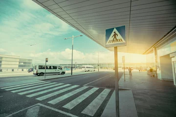Papier Peint photo Aéroport Pedestrian crossing area next to modern contemporary airport terminal entrance, zebra traffic cross way with road sing with parking lot and small buses in distance on sunny day in Barcelona, Spain