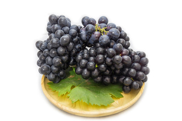 Black grapes bunch isolated on wooden plate and white background with green leaf package design element
