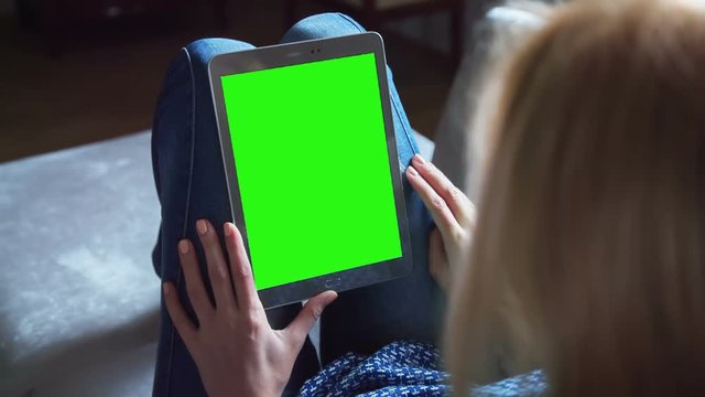 Young Woman in blue jeans sitting on couch uses Tablet PC with pre-keyed green screen. Few types of gestures - scrolling up and down, tapping, zoom in and out. Perfect for screen compositing