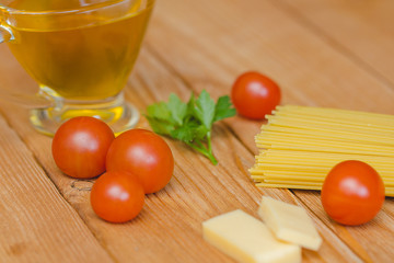 Паста лежит на столе рядом с черри  и сыром, рядом стоит соусник с оливковым маслом.