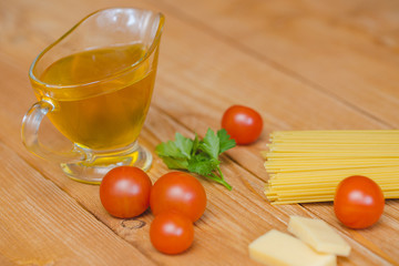 Паста лежит на столе рядом с черри  и сыром, рядом стоит соусник с оливковым маслом.