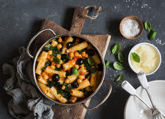 Rigatoni pasta with chickpeas, spinach and olives in a tomato sauce on a dark background, top view. Vegetarian food concept