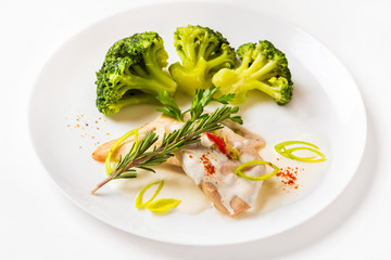 Plate of steamed chicken and broccoli with white sauce isolated.