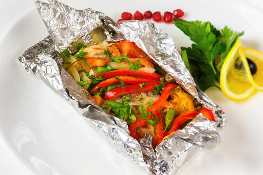 White fish fillet baked in foil with vegetables on a plate at isolated background.