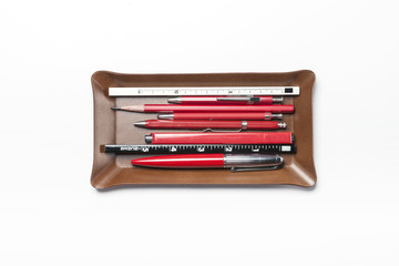 A brown leather pencil tray with red pencil isolated white.