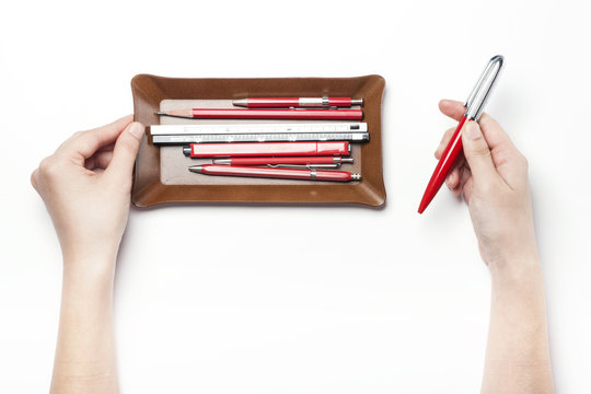 A Woman Hand Hold A Red Pen With Brown Leather Pencil Tray Isolated White.