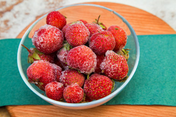 rozen strawberries are medium in size in a glass container on a wooden stand