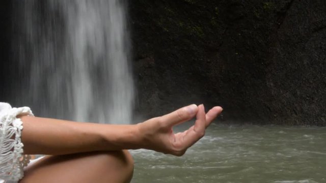 woman doing sitting meditation at waterfall in the tropics