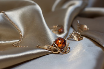 Closeup gold chain with pendant from gold and authentic baltic amber on light brown atlas. Gold...