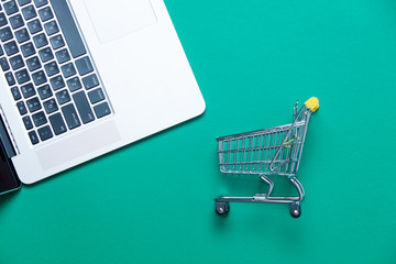 beautiful small shopping cart and modern silver laptop on the wonderful blue background