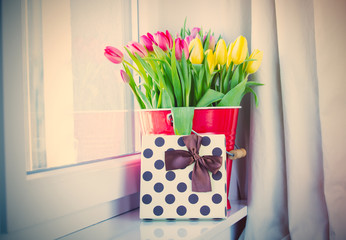bunch of beautiful colorful tulips in red bucket  and cute gift on the wonderful windowsill