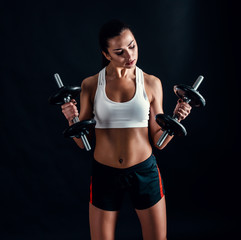 Fototapeta na wymiar Athletic young woman doing a fitness workout against black background. Attractive fitness girl pumping up muscles with dumbbells.