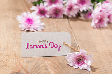 Womans Day tag paper with color flowers on wooden background. Top view.