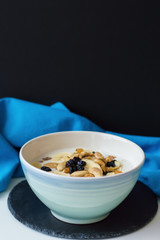 Vertical photo of blue bowl with oatmeal porridge topped with banana slices, raisin and nuts on black slate board. Healthy breakfast concept