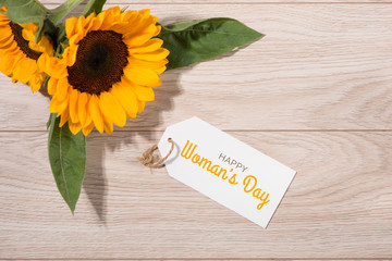 Womans Day tag paper with yellow flowers on wooden background. Top view.