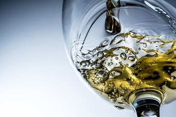 Stream of white wine pouring into a glass, white wine splash on grey background