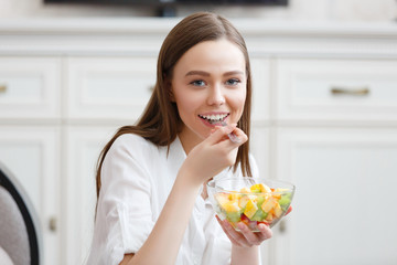 Young woman eating healthy fruit breakfast in bowl at home