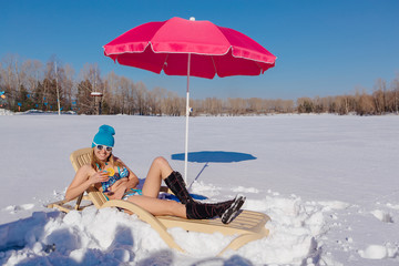Beautiful girl relaxing on the sunbed on the winter snowy beach.
