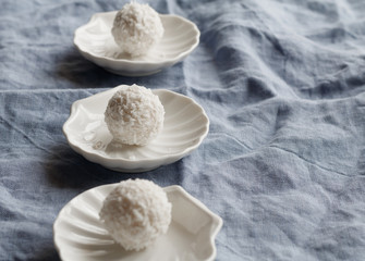Close-up of white coconut candy in the shape of a ball on a white saucer in the form of shells on blue background.