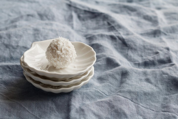 Close-up of white coconut candy in the shape of a ball on a white saucer in the form of shells on blue background.