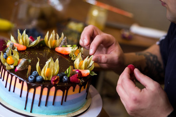 Pastry chef in the kitchen decorating a cake of chocolate,fruit,candies,Confectioner is decorating chocolate cake,cooking class, culinary, bakery, food and people concept