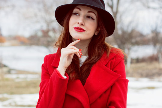 Beautiful french stylish  woman  in black hat and red coat walking in park