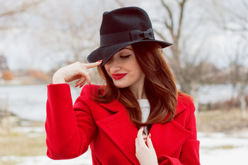 Beautiful french stylish  woman  in black hat and red coat walking in park