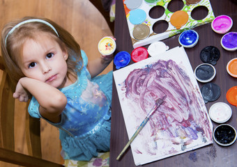 The child is engaged in creativity, the girl draws paints