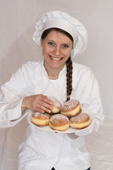 Junge Konditorin lächelt und präsentiert Krapfen