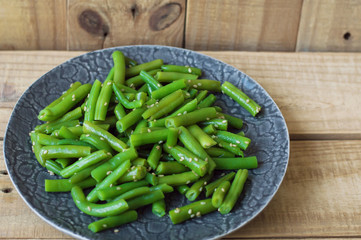 Plate with cooked green beans with sesame seeds on wooden background