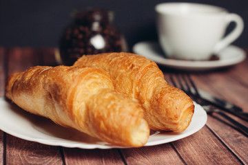 Fresh croissants on a plate, a drink in a cup and coffee beans in a jar