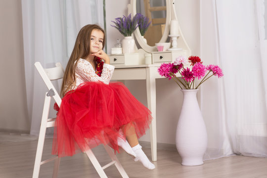 little girl sitting on a wooden chair. A child in a red skirt