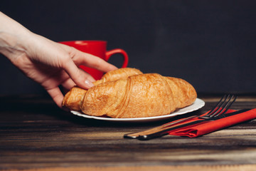 hand and croissants in a plate, red mug
