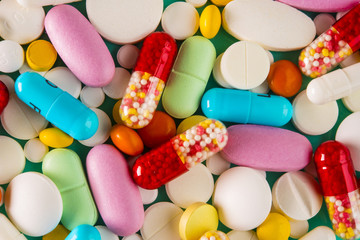 Multicolored pills and tablets on green background, top view