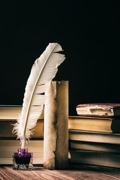 Literature concept. Old inkstand with feather near scroll and books on black background. Vintage toned image.