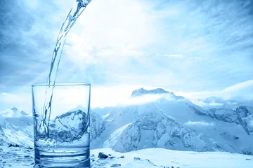 Abwaschbare Fototapete Wasser Konzept Reinheit des blauen Wassers in transparentem Glas über Winterlandschaft der Berge höher als Wolken, Nahaufnahme