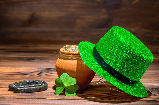St Patricks day concept with pot full gold coins, horseshoe, green hat and shamrock on vintage wooden background, close up