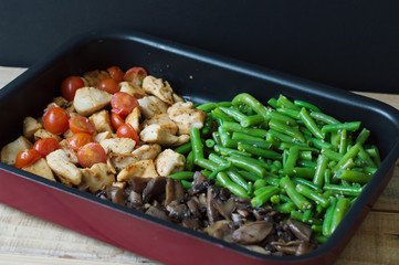 Mix of cut chicken breasts, green beans with sesame, cherry tomatoes and champignon mushrooms baked in a metal pan