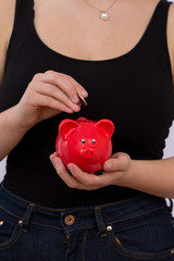 junge Frau steckt Euro Münze in rotes Sparschwein