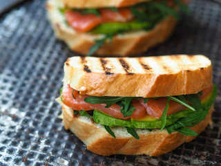 Two homemade sandwich with avocado, salmon and arugula on  old metal  background
