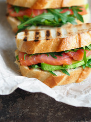 Two homemade sandwich with avocado, salmon and arugula on a dark background
