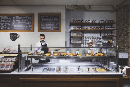 Man and woman bakers working in bar behind pastry showcase.